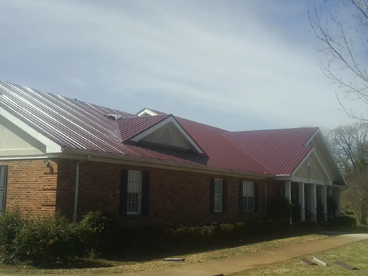 Red metal roof with gabled entries on a long brick building, from a Hail Damage Roof Repair job in Dagsboro