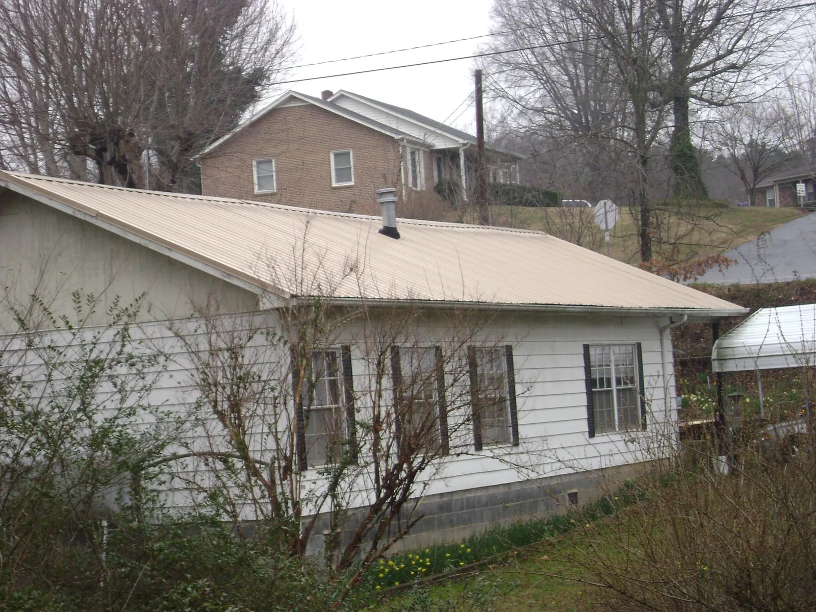 Tan metal roof on a white sided house set into a hillside — Commercial Roofing by Roofing Brothers in Dagsboro